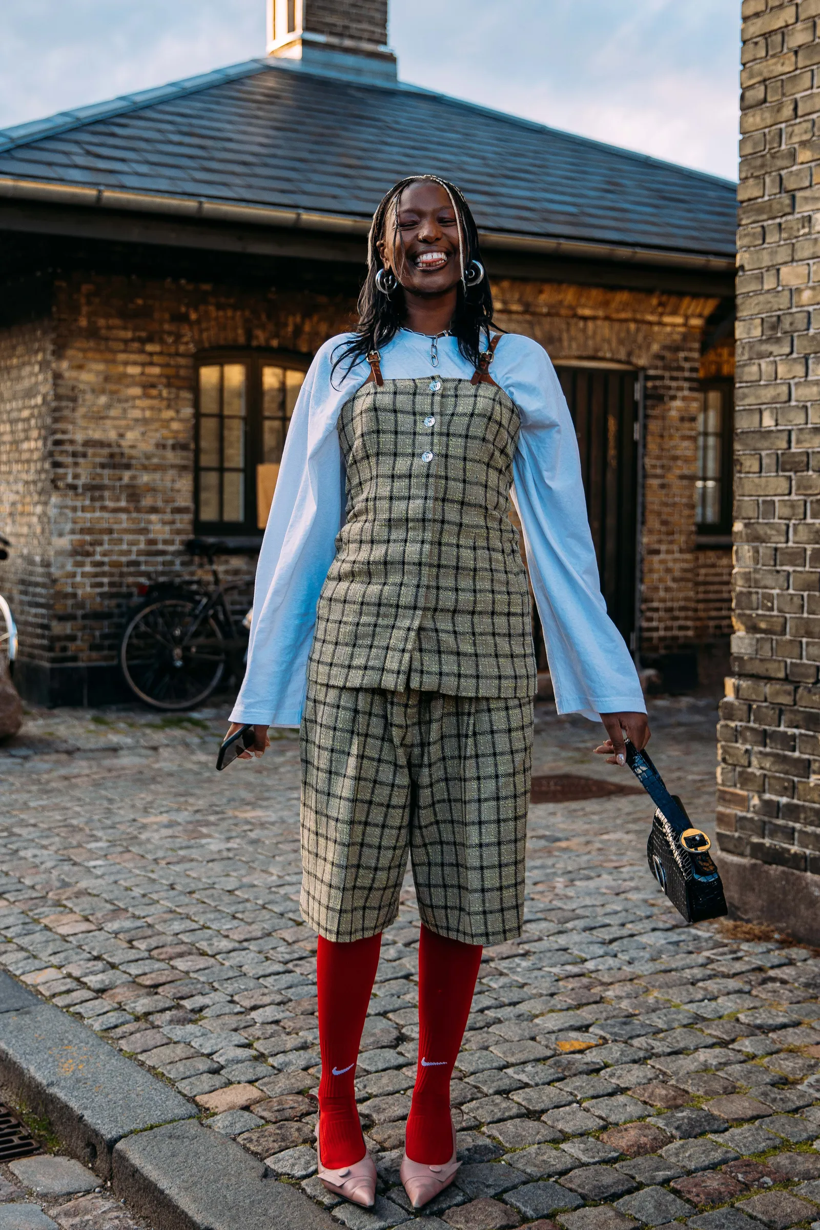 Oversize’owa niebieska koszula to hit w połączeniu z retro kompletem w kratę. Nieoczywistym zwieńczeniem stylizacji okażą się piłkarskie skarpety Nike w czerwonym kolorze oraz różowe baleriny z noskiem w szpic.