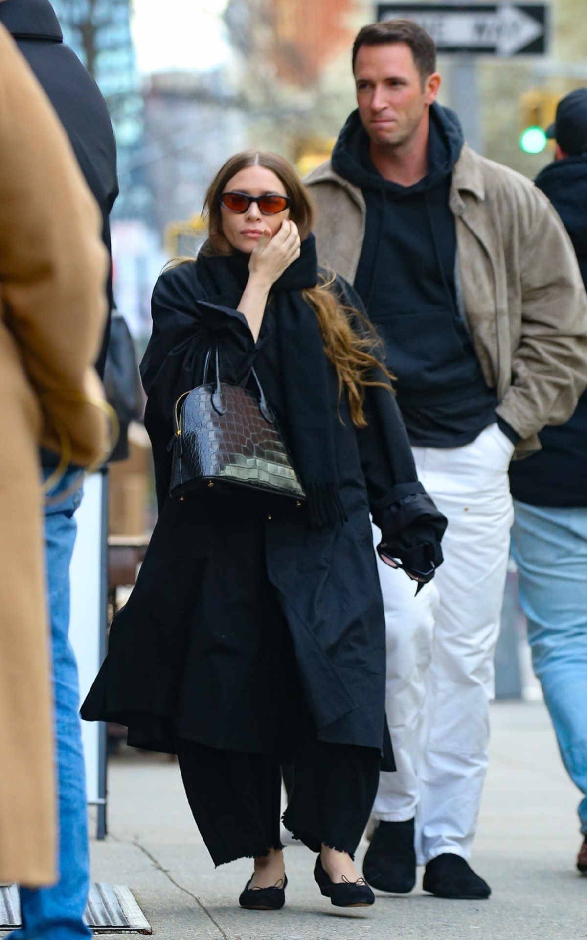 Ashley Olsen w czarnych balerinkach, czarnym płaszczu, z czarną torebką i w okularach przeciwsłonecznych z kolorowymi szkłami.