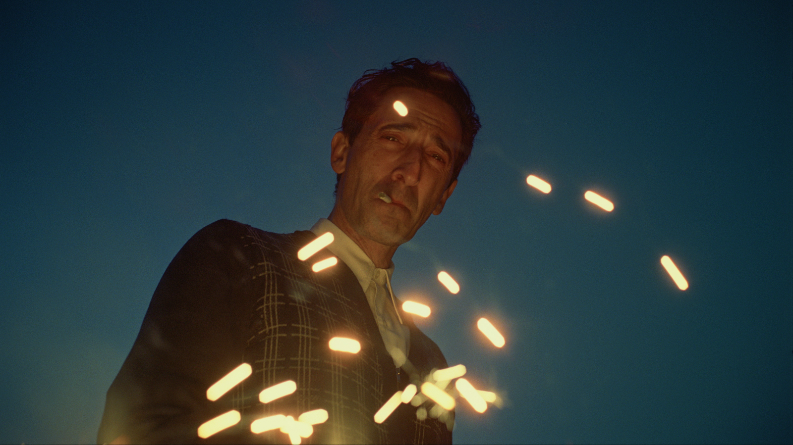 Adrien Brody w filmie „The Brutalist”, z papierosem, z efektem świetlnym w tle.
