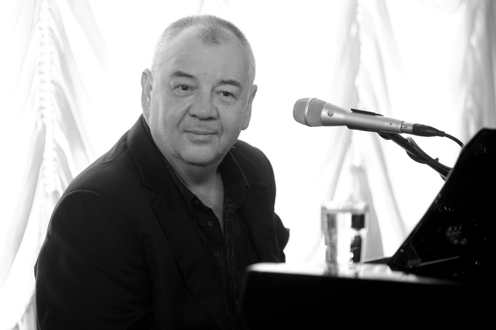 Stanisław Soyka w czarnej koszuli przy fortepianie.