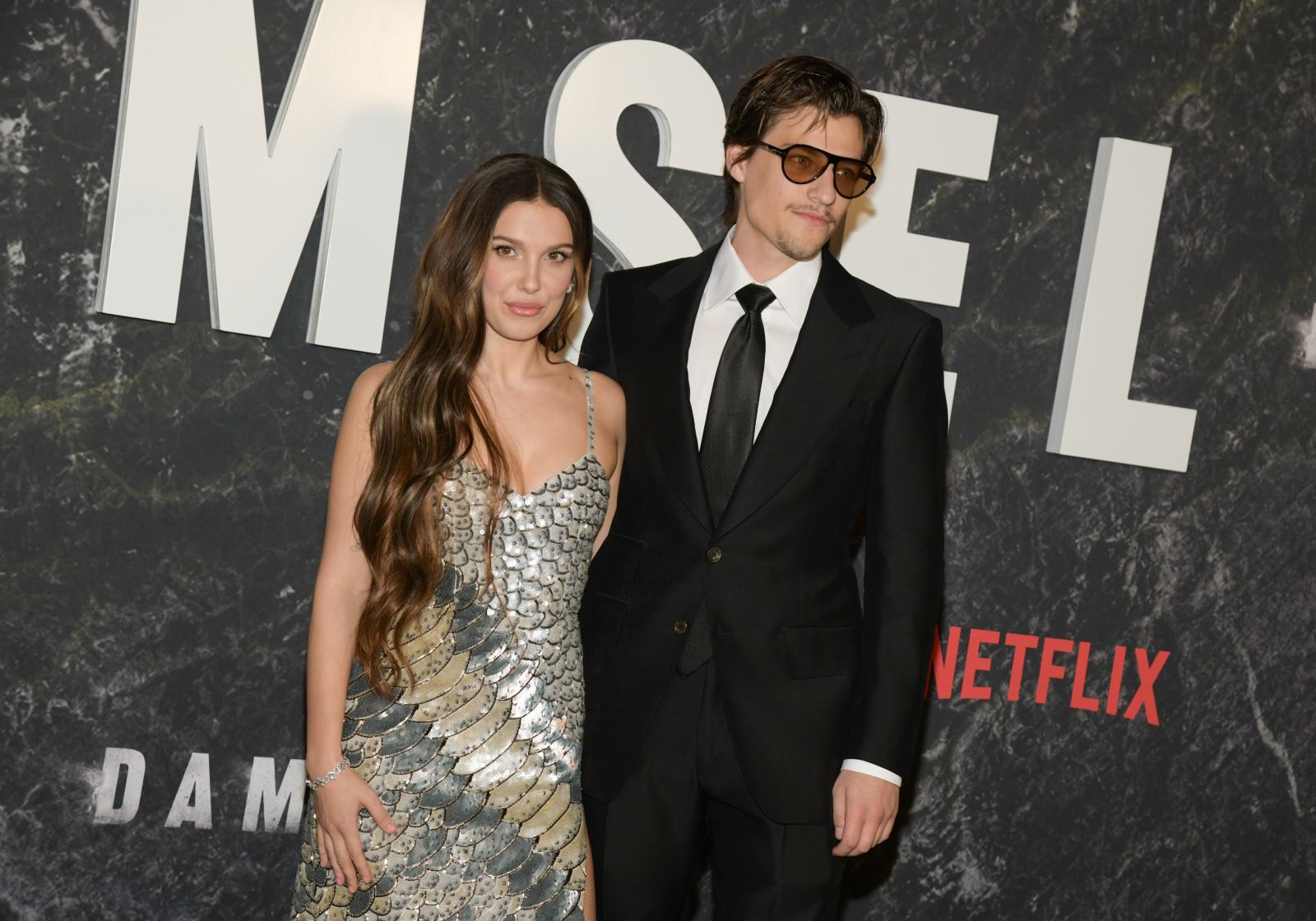 Millie Bobby Brown i Jake Bongiovi na premierze w 2024 roku, ubrani elegancko na tle napisu "MSELM".