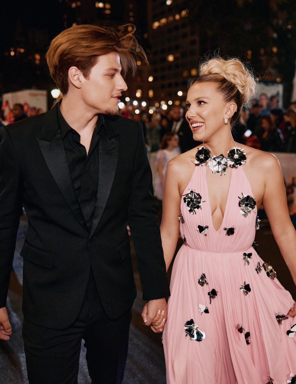 Jake Bongiovi i Millie Bobby Brown podczas wydarzenia w 2022 roku, idą ręka w rękę, uśmiechając się do siebie.