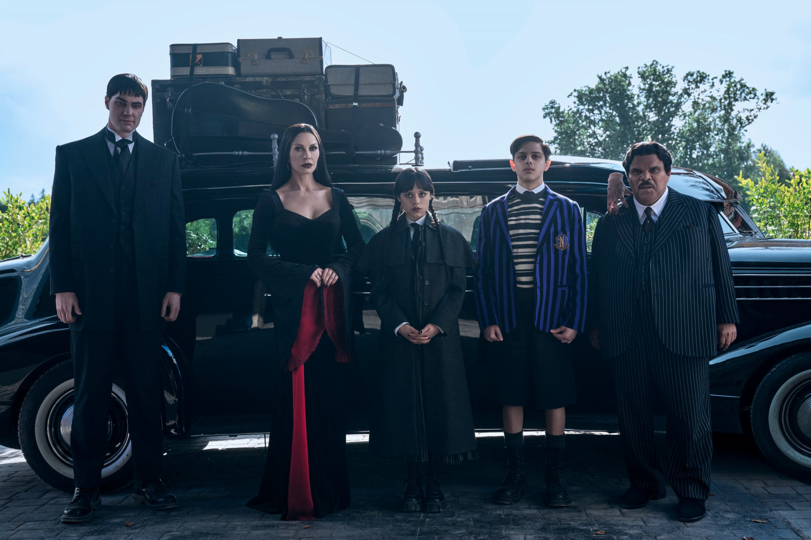 Rodzina Addamsów w drugim sezonie serialu Netflix „Wednesday” stoi przy czarnym samochodzie z bagażem.