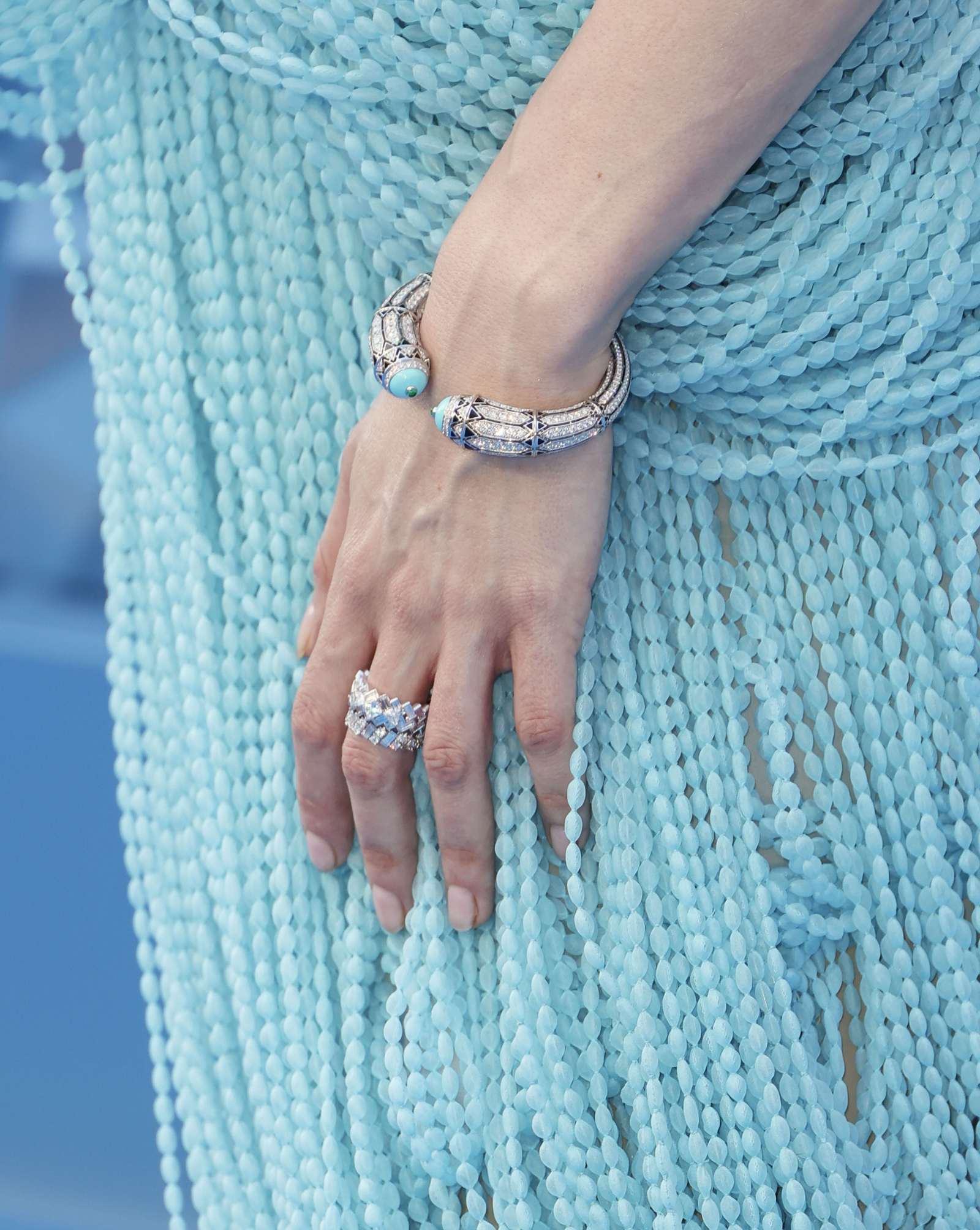 Vanessa Kirby prezentuje srebrną bransoletkę z turkusami oraz pierścionek, w tle zwiewna, niebieska kreacja.