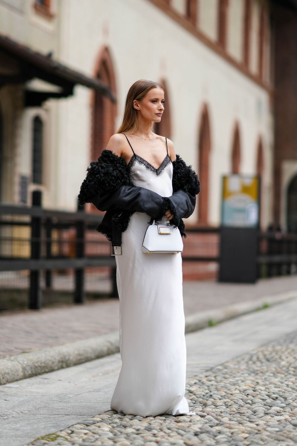 Kobieta w satynowej sukience slip dress i skórzanej kurtce damskiej spaceruje po ulicy.