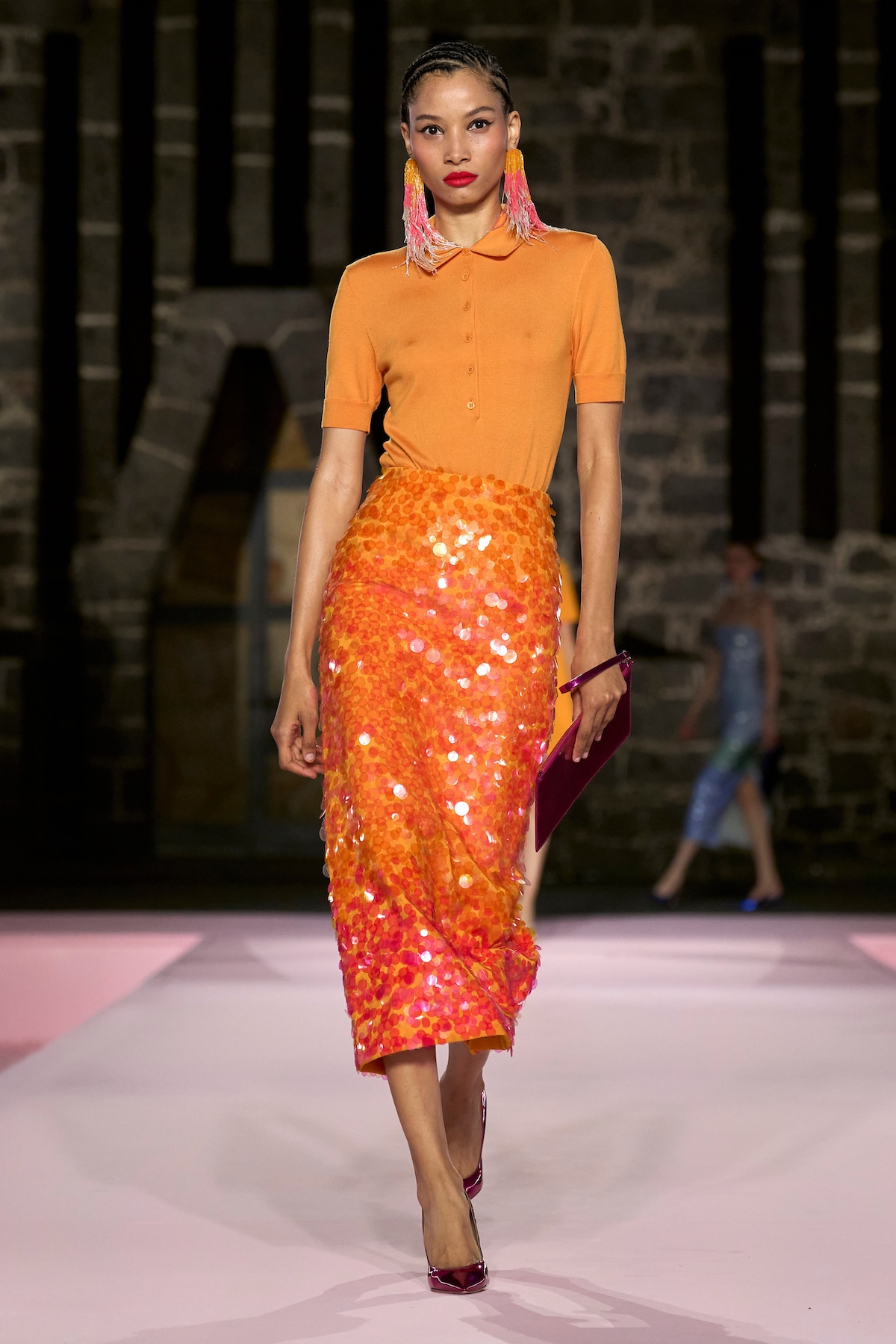 Modelka w pomarańczowym topie i cekinowej spódnicy midi w kolorze pomarańczowym na pokazie Carolina Herrera Resort 2026.