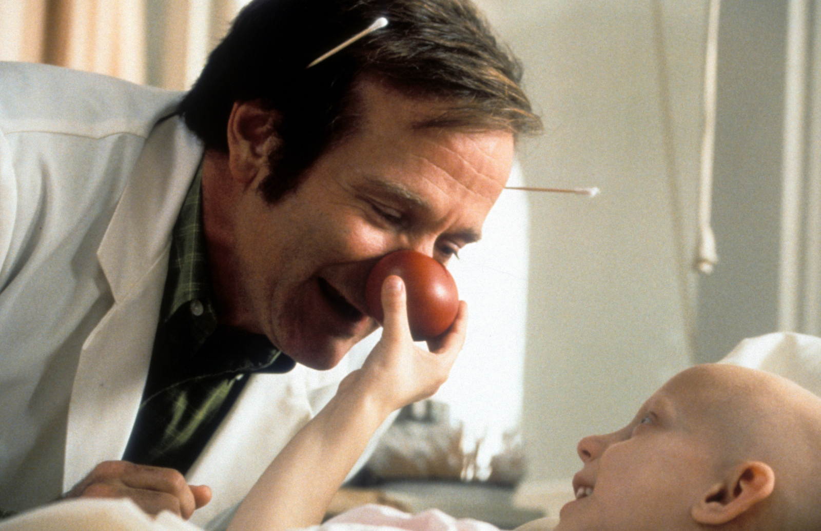 Robin Williams w filmie „Patch Adams” bawi się z dzieckiem w szpitalu, używając czerwonego nosa.