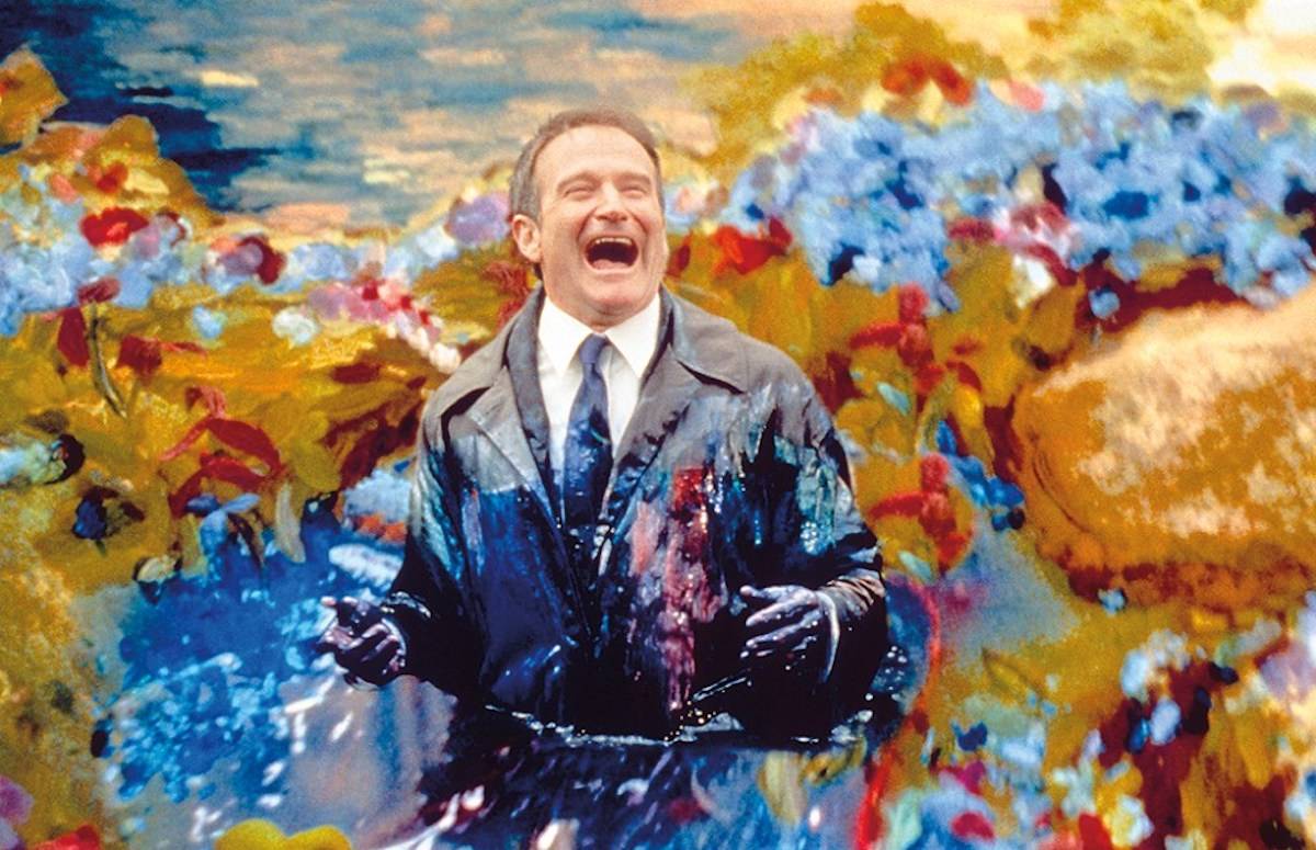 Robin Williams w filmie „Między niebem a piekłem” z uśmiechem, zanurzony w kolorowym, malarskim tle.