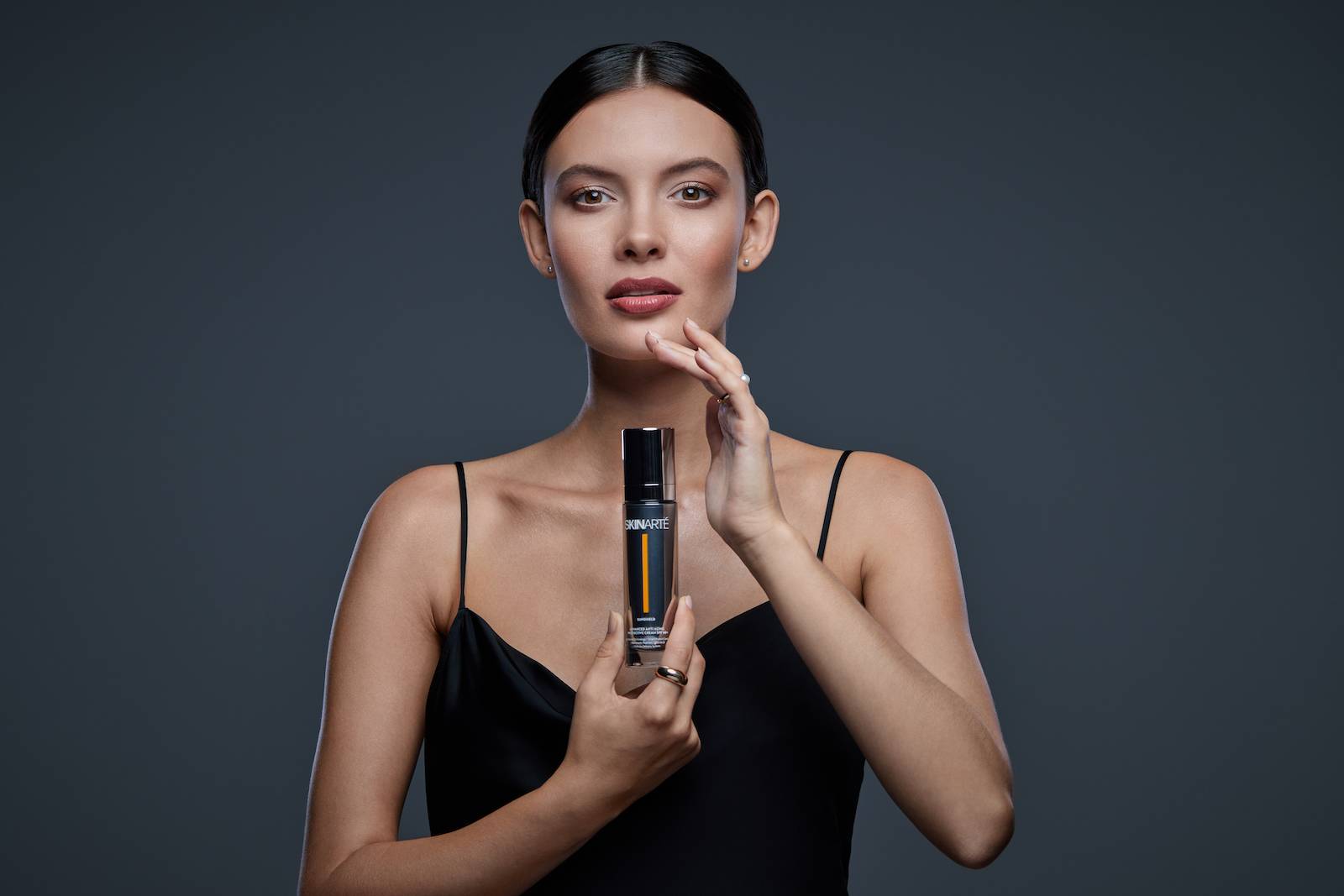 Modelka w czarnej sukience, trzymająca w dłoniach krem Skinarte.